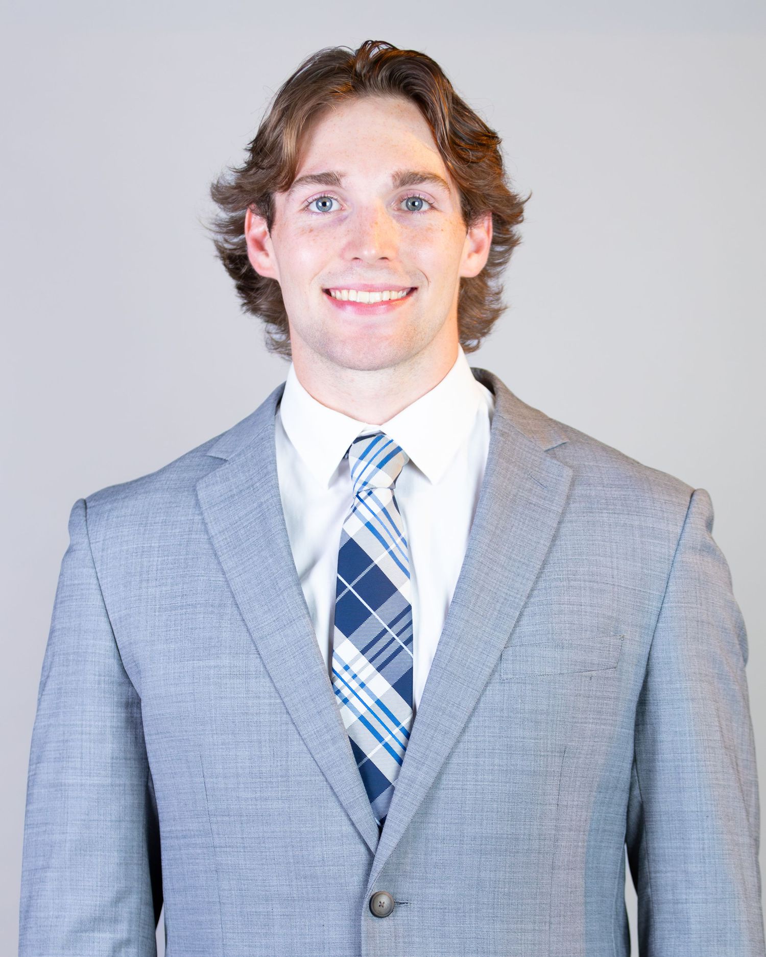 Professional headshot of someone in a light gray suit and blue striped tie against a neutral background.