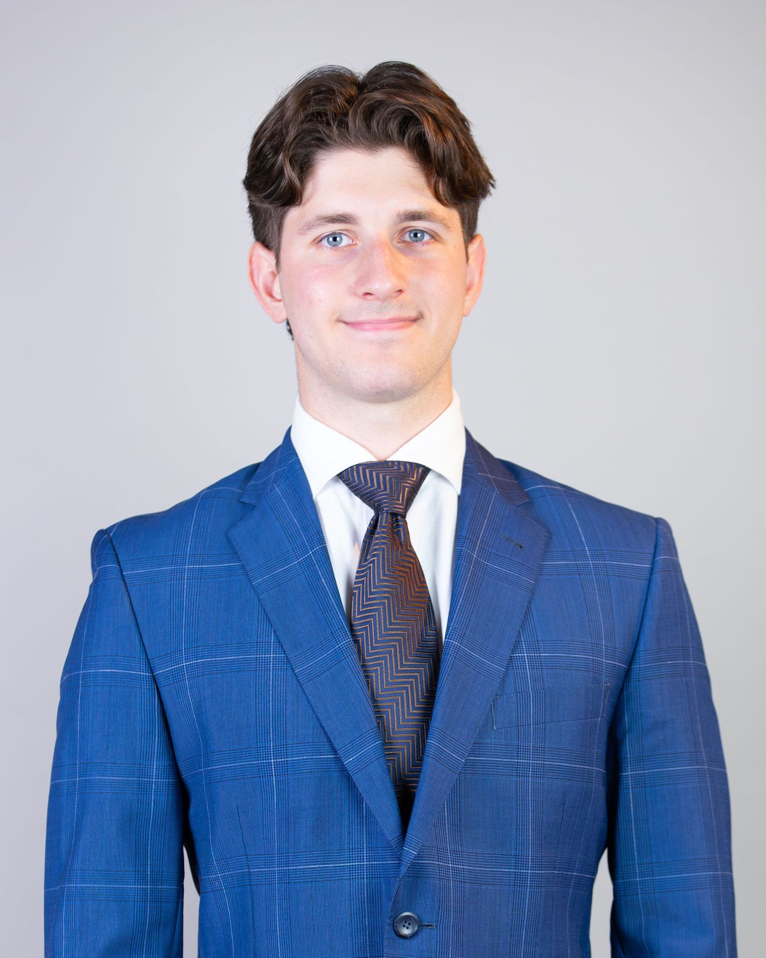 Professional wearing a tailored blue windowpane suit with navy tie stands against light background.