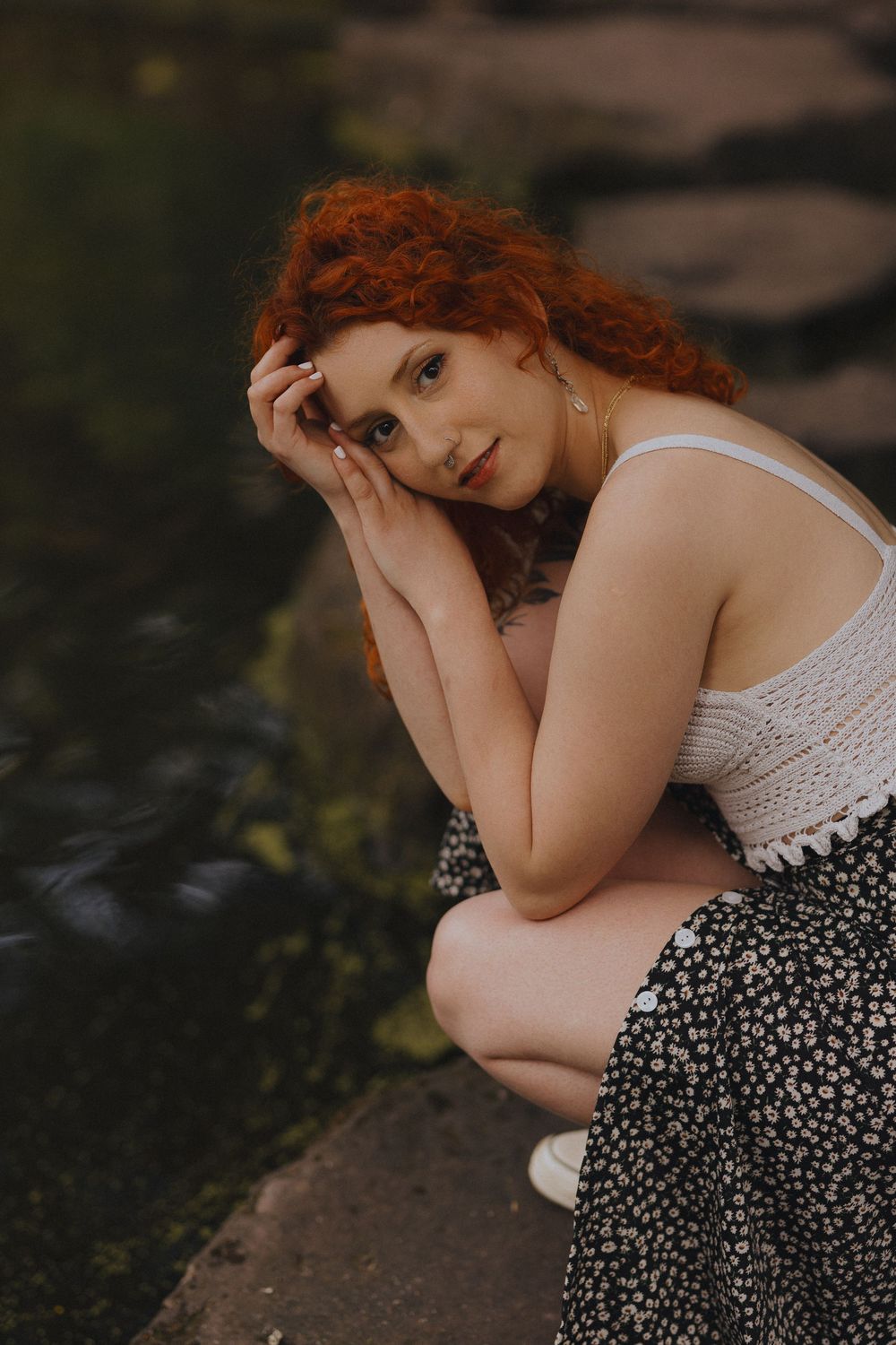 A dreamy outdoor portrait featuring someone in a white lace top and floral dress resting against a rock.