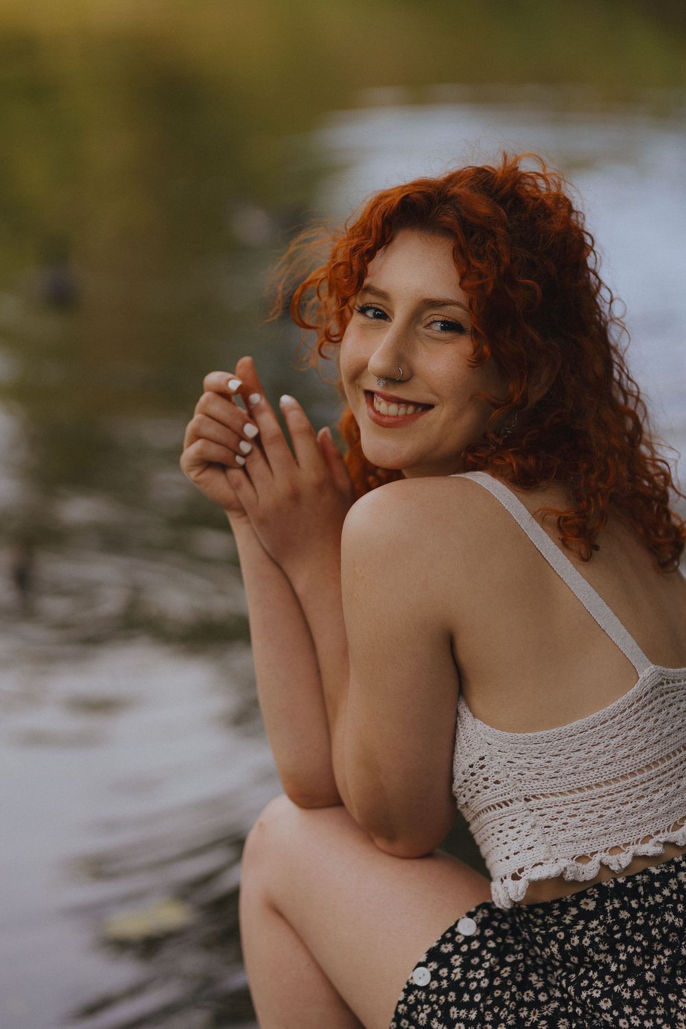 A dreamy portrait by the water featuring flowing red curls and a crochet top with floral print.