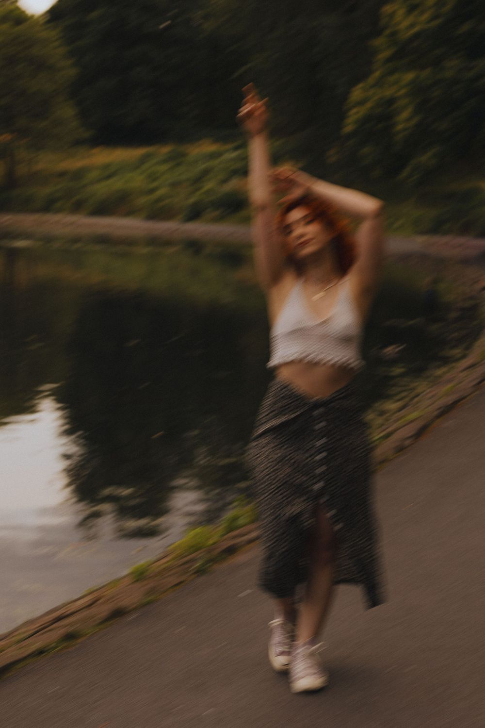 Blurred motion sequence of person in casual attire dancing by a serene lake at sunset.