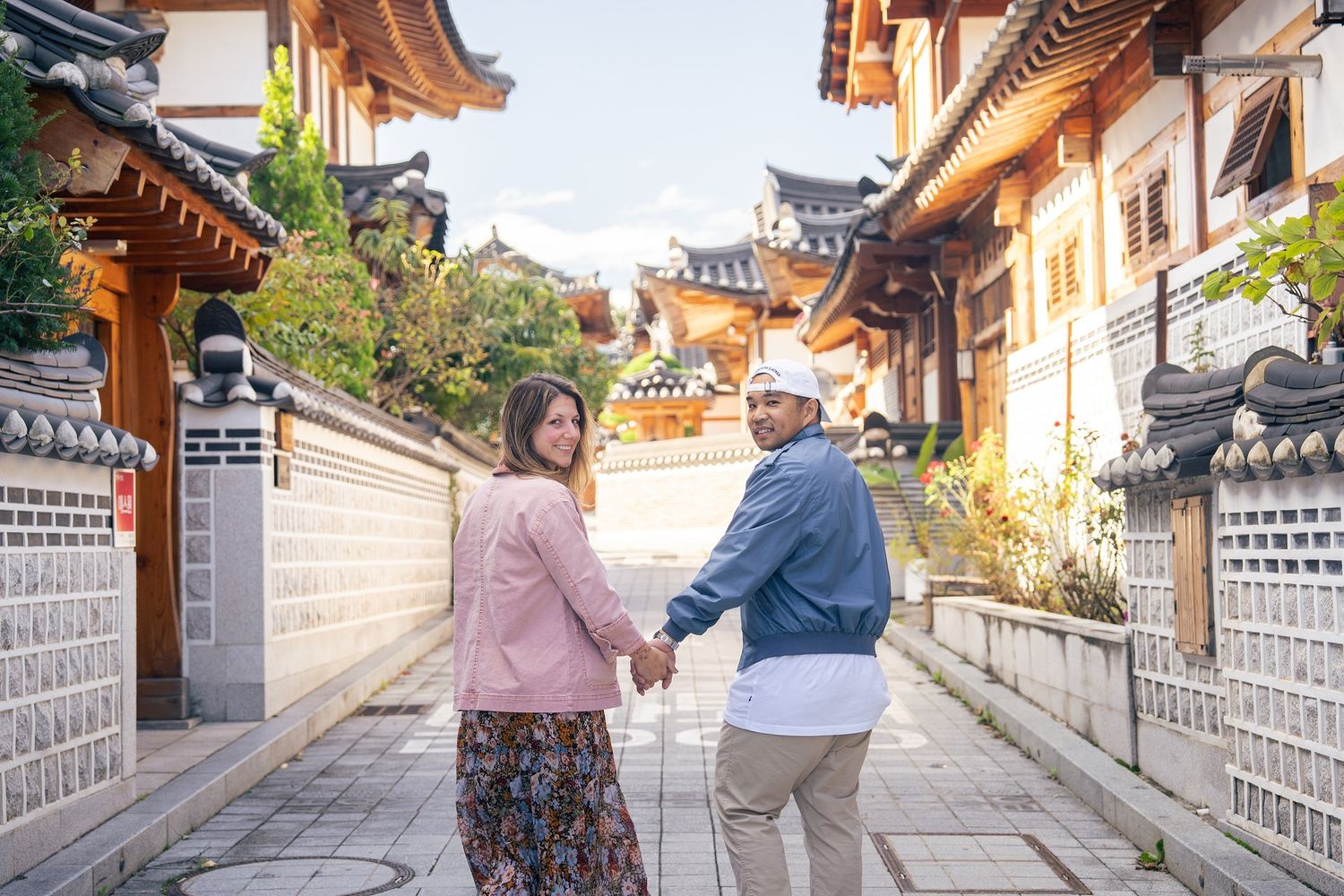 Traditional Korean hanok village street with stone walls and tiled roofs in warm sunlight during autumn season.