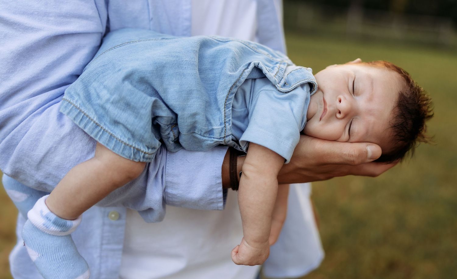Close-up shot of hands tenderly holding a sleeping infant in denim clothing.