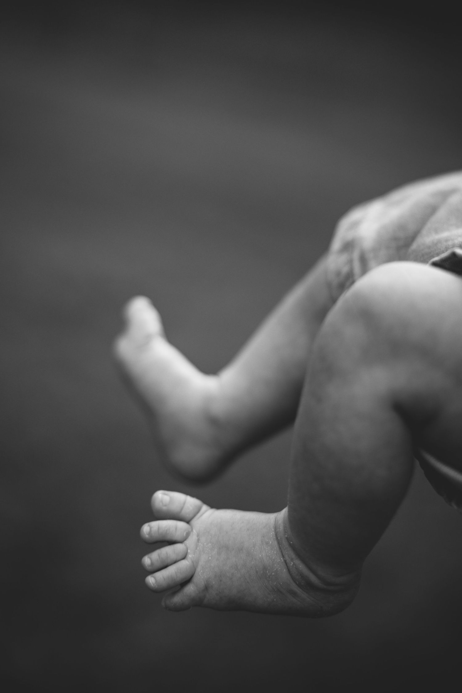 Close-up black and white photo of tiny baby feet and toes against dark background.
