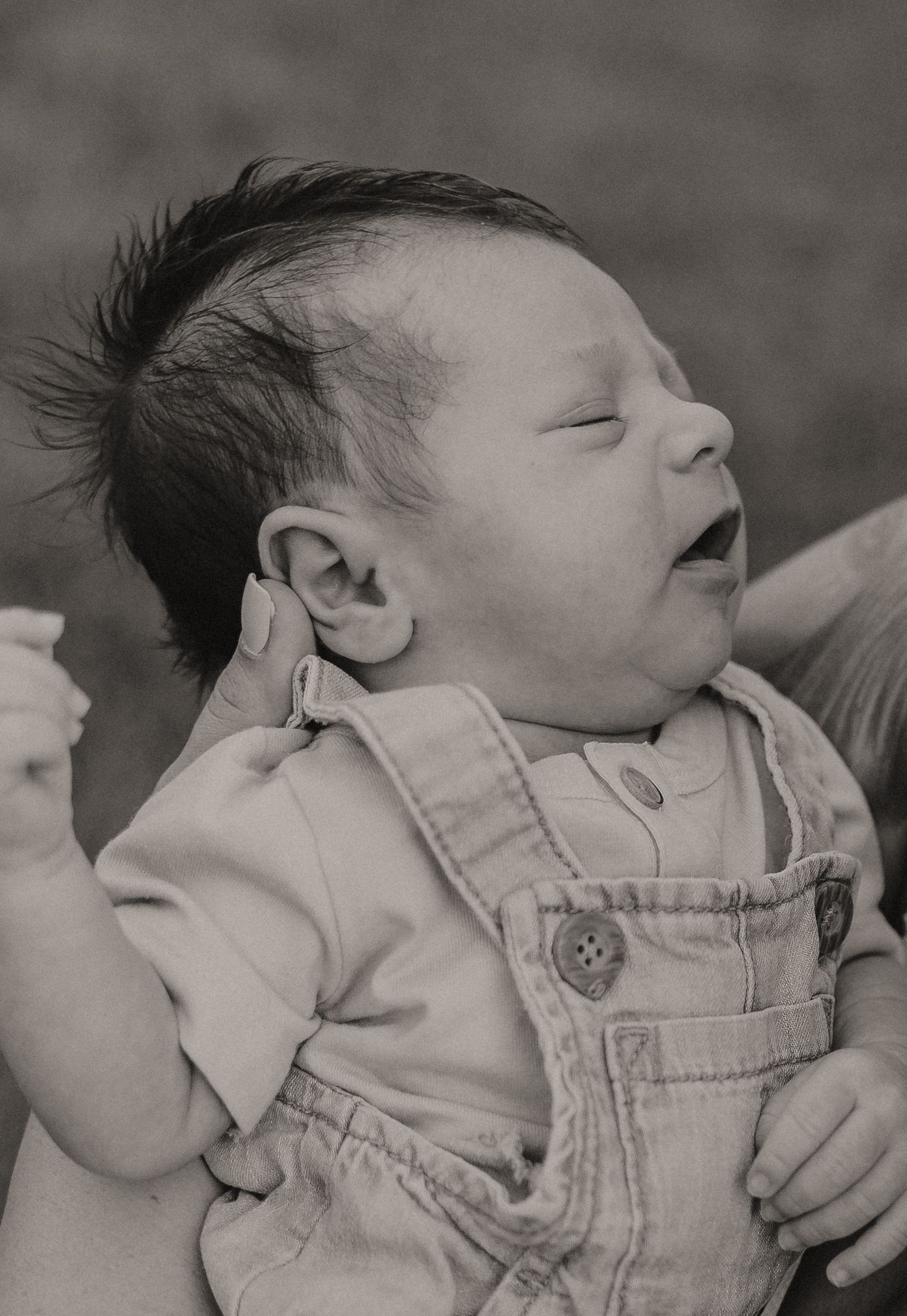 Black and white portrait of sleeping infant in overalls with spiky hair.