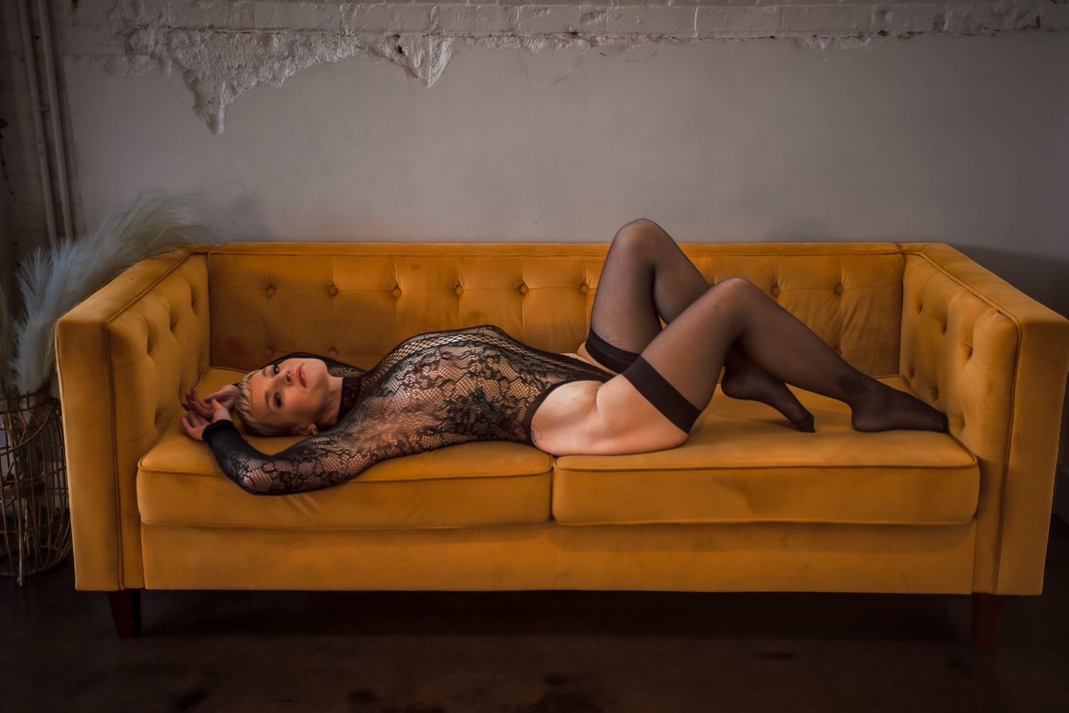 Boudoir photography of a confident woman wearing a black bodysuit, reclining on a bright yellow couch in a studio setting in Salt Utah