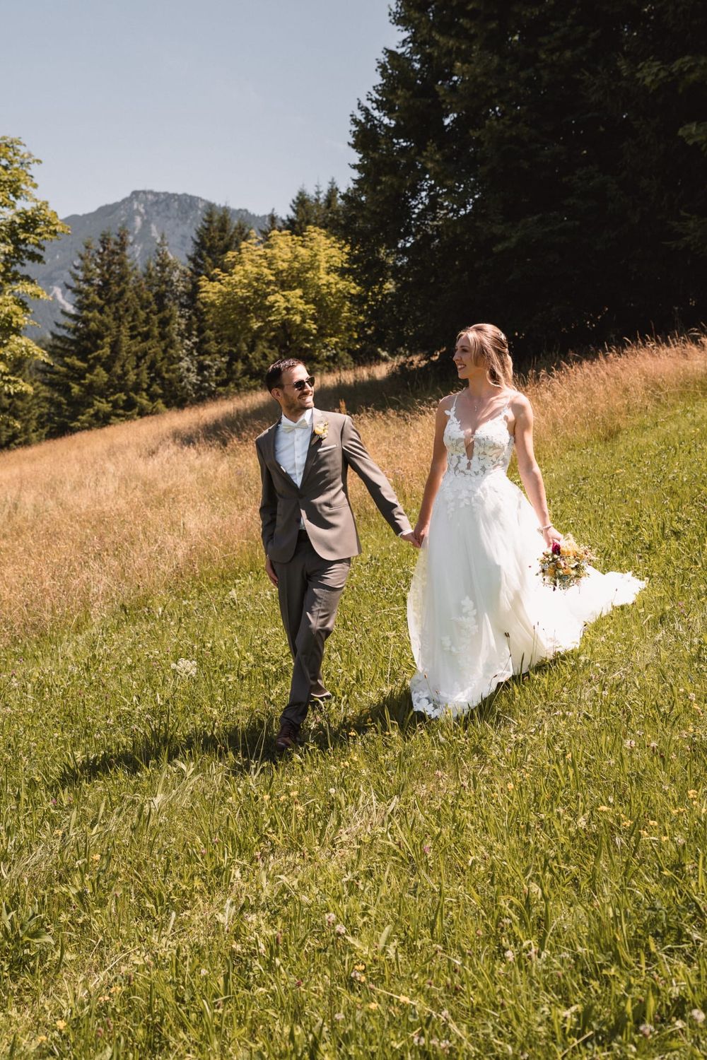 Wedding couple walking through sunny mountain meadow on their special day.