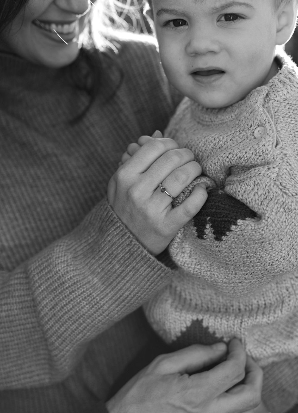 A black and white close-up photo showing hands clasped together while wearing cozy knit sweaters.
