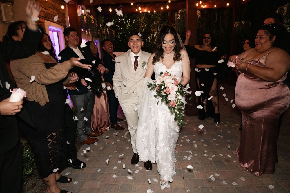 Wedding celebration at night with guests throwing petals as couple walks through under string lights.