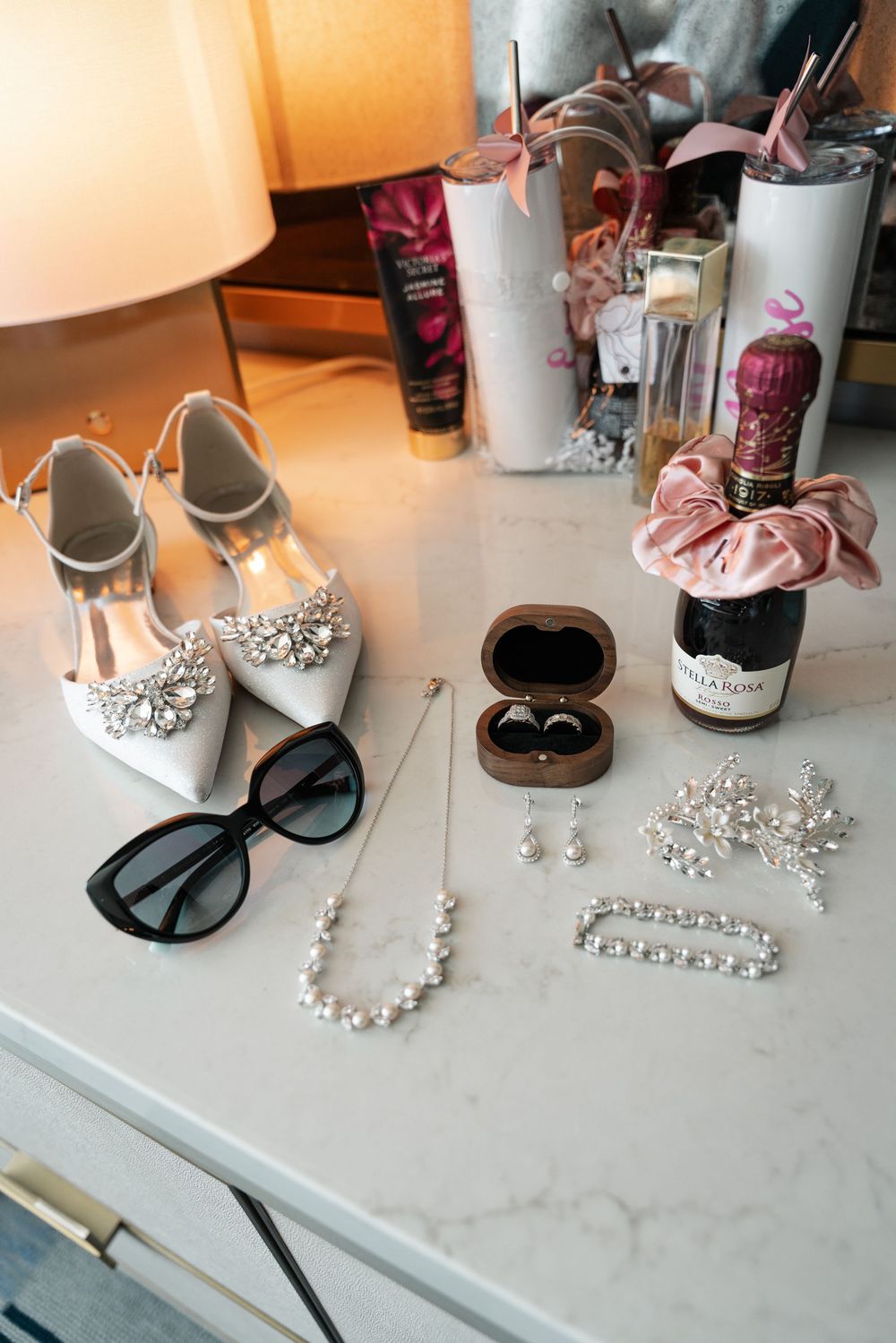 Elegant white bridal shoes displayed with pearl jewelry and sunglasses on a marble surface.
