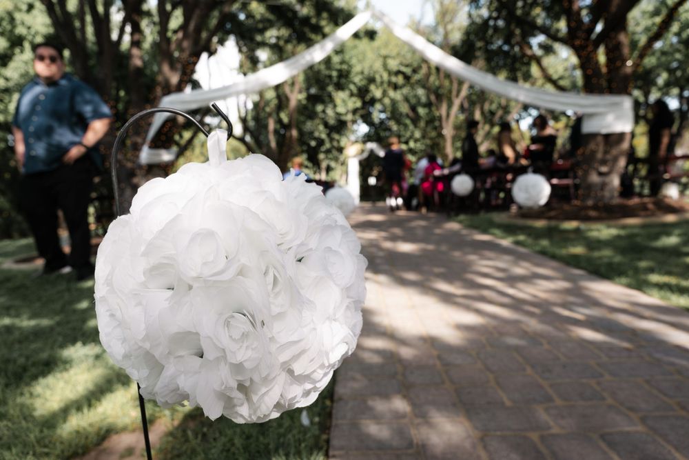 A wedding ceremony setup in a garden with white chairs and floral decorations along a brick pathway.