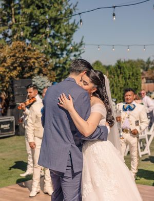 Wedding couple shares first dance outdoors while guests in cream-colored attire watch.