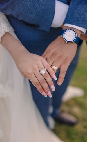 Close-up of hands wearing wedding rings and blue suit details.