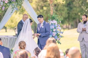 Outdoor wedding ceremony under a floral arch with guests watching.