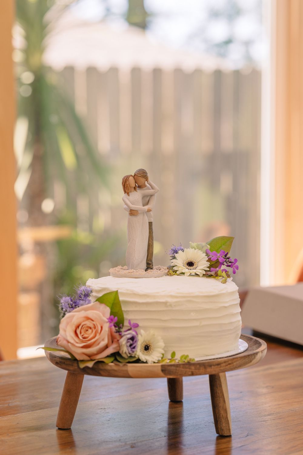 White frosted wedding cakes decorated with fresh flowers displayed on wooden pedestals.
