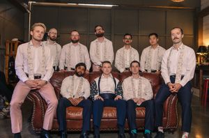 Groomsmen in matching pink shirts and suspenders pose together on vintage leather furniture.