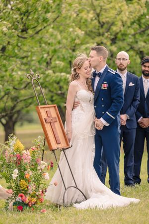 Newlyweds kiss under a draped wedding arch decorated with colorful flowers in a garden setting.