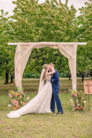A romantic dip kiss between newlyweds in a blooming flower field with mountains in the background.