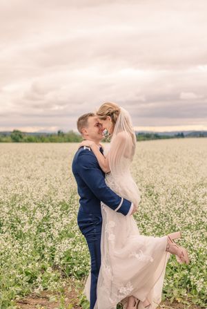 A couple shares an intimate moment in a field of white flowers under cloudy skies.
