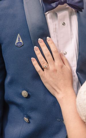 Close-up of hands wearing wedding rings against a navy blue suit jacket.