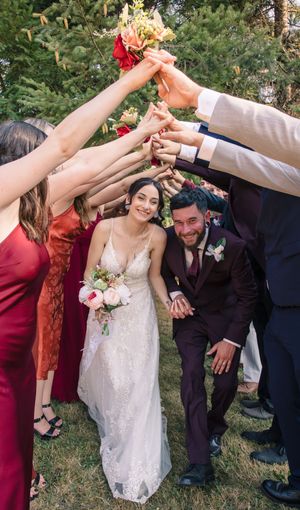 Wedding guests form a tunnel of raised arms over the newlyweds during outdoor celebration.