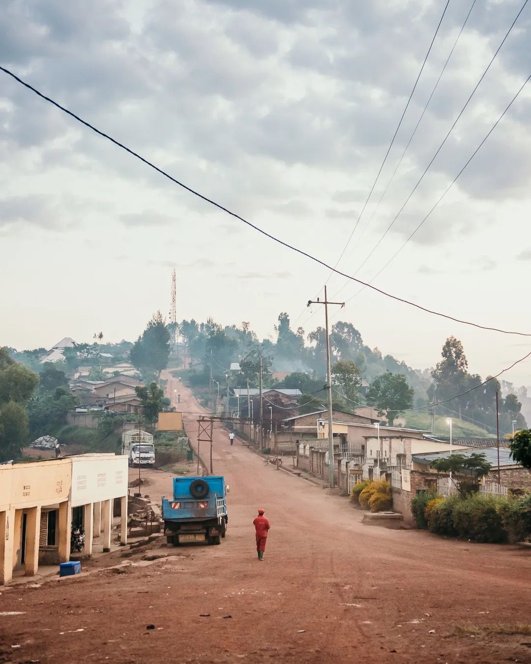 People and vehicles move along a red dirt road in a busy town, capturing daily life, local transport and community activity.