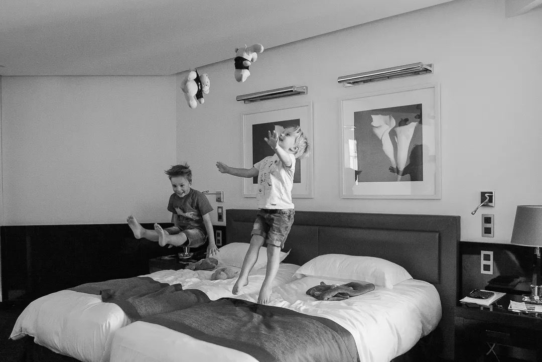Two children jumping on a hotel bed in a playful black-and-white moment.