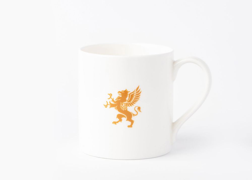 White ceramic coffee mug with small orange lion logo design against white background.