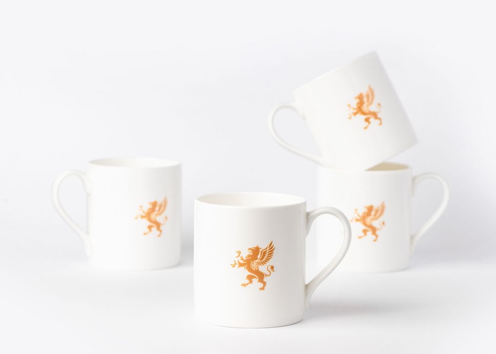 Four white ceramic coffee mugs with orange lion designs arranged on a white background.