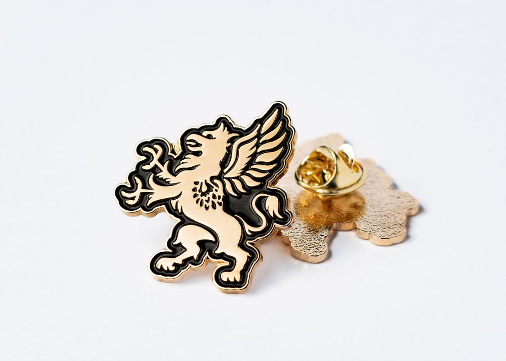 Gold and black enamel griffin lapel pin with wing details and metallic finish.