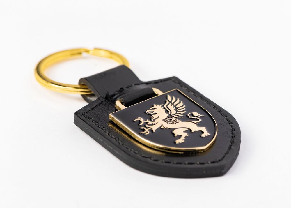Black leather keychain with gold-trimmed shield emblem featuring a rampant lion design on dark background.
