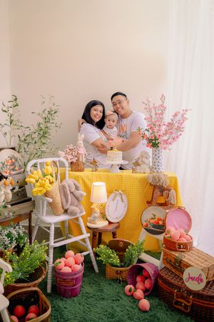 Baby photo session setup with yellow backdrop, floral decorations, and vintage props on artificial grass.