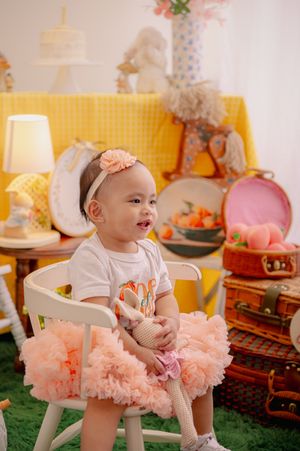 Baby in white outfit and peach tutu posing in decorated studio setting.