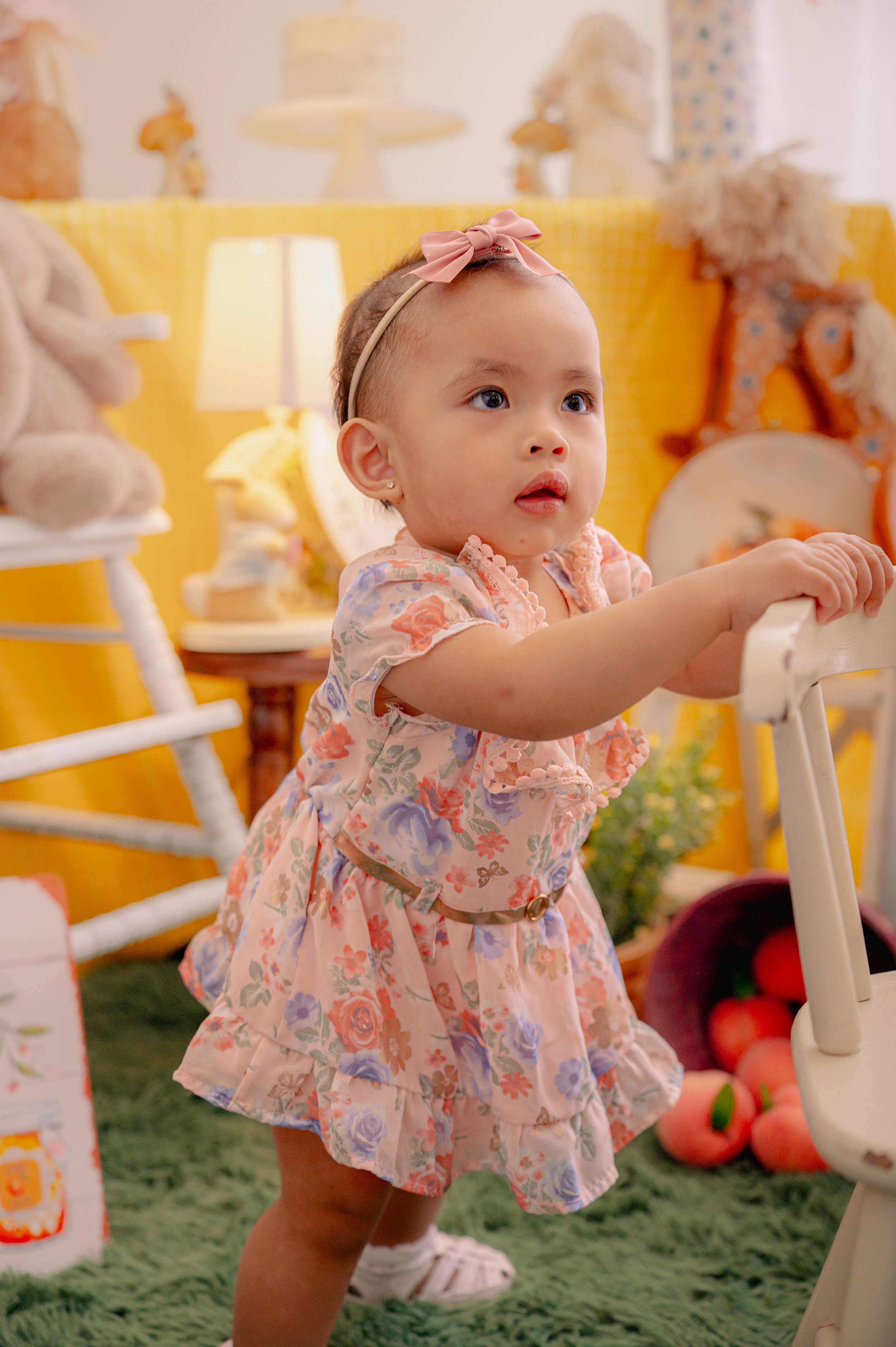 Baby in floral dress playing on green carpet with white furniture and yellow walls.