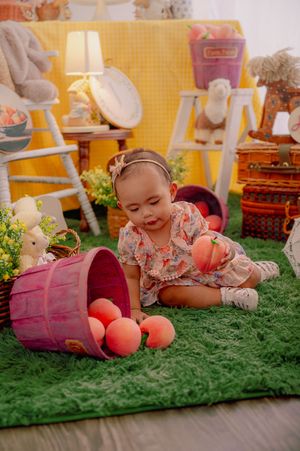 Baby playing on green carpet with pink decorative elements and fruit props.