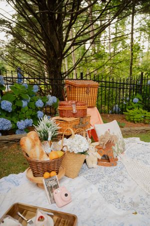 Garden picnic setup with white lace blanket, wicker baskets and blue hydrangeas.