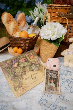 Vintage-style picnic display with wicker baskets, bread, flowers and decorative cards on a lace tablecloth.