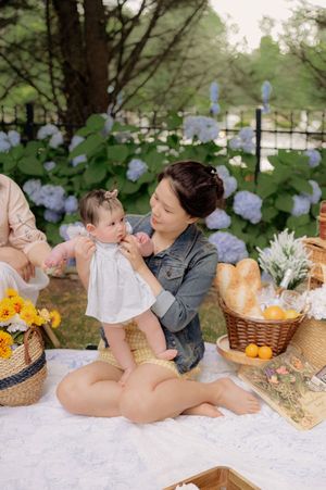 Picnic scene with fresh flowers, wicker baskets and citrus fruits on white blanket.