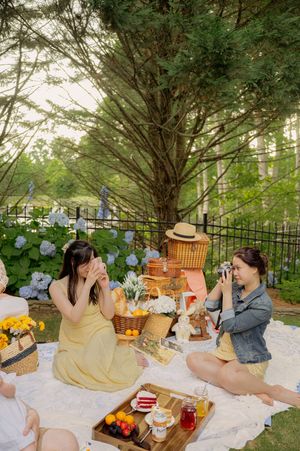Friends enjoying an outdoor picnic with snacks and drinks under trees and blue hydrangeas.