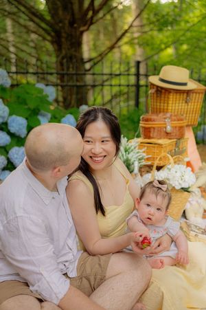 Outdoor family picnic with wicker baskets and fresh flowers under pine trees.