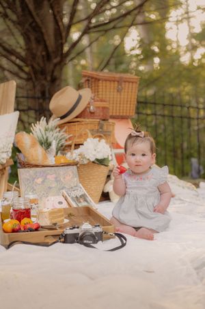 Garden picnic setup with vintage camera, fresh strawberries, and wicker baskets on white blanket.