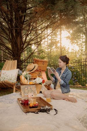 A dreamy summer picnic scene with books, drinks and snacks laid out on a white blanket at sunset.