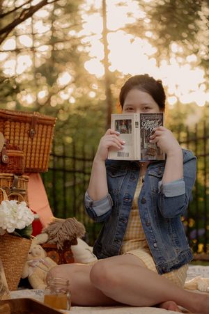 A cozy picnic setup featuring someone reading a book while relaxing on a blanket outdoors.
