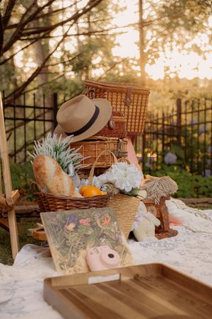 A vintage-style picnic setup with wicker baskets, straw hat, and fresh bread on a white blanket.