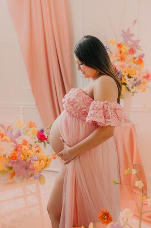 Elegant maternity session with flowing pink gown and colorful floral arrangements.