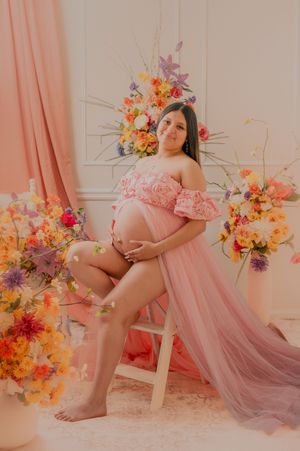 Dreamy maternity photos with soft pink tulle dress and vibrant flower decorations.