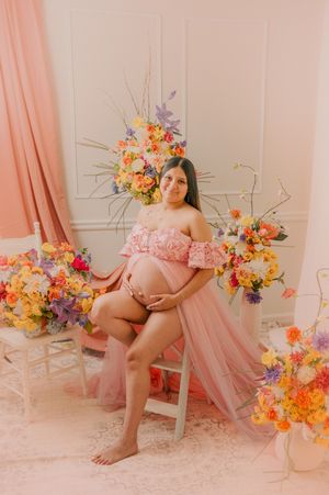 Romantic maternity portrait with pink draping and bright floral arrangements.