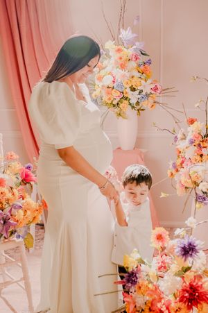 Elegant white maternity gown photoshoot with colorful flower decorations.