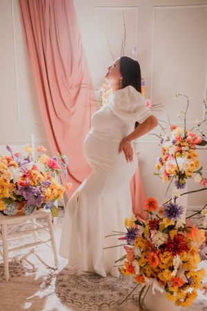 Artistic maternity session featuring white gown and vibrant flower arrangements.