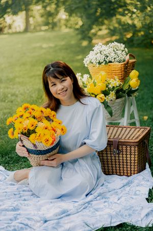 Outdoor photoshoot with blue dress, yellow flowers and picnic setup on grass.
